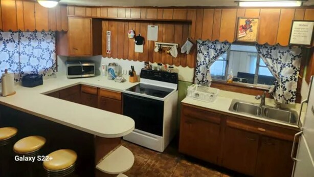 Cocina compacta con armarios de madera, microondas, estufa, pileta y taburetes.
