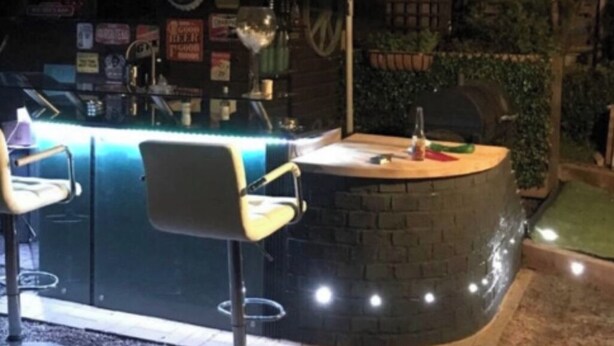 An outdoor bar area with a circular stone counter, two bar stools, and an umbrella providing shade. - Beautiful 1-bed Secluded Cabin, With bar & Fire (Godstone)