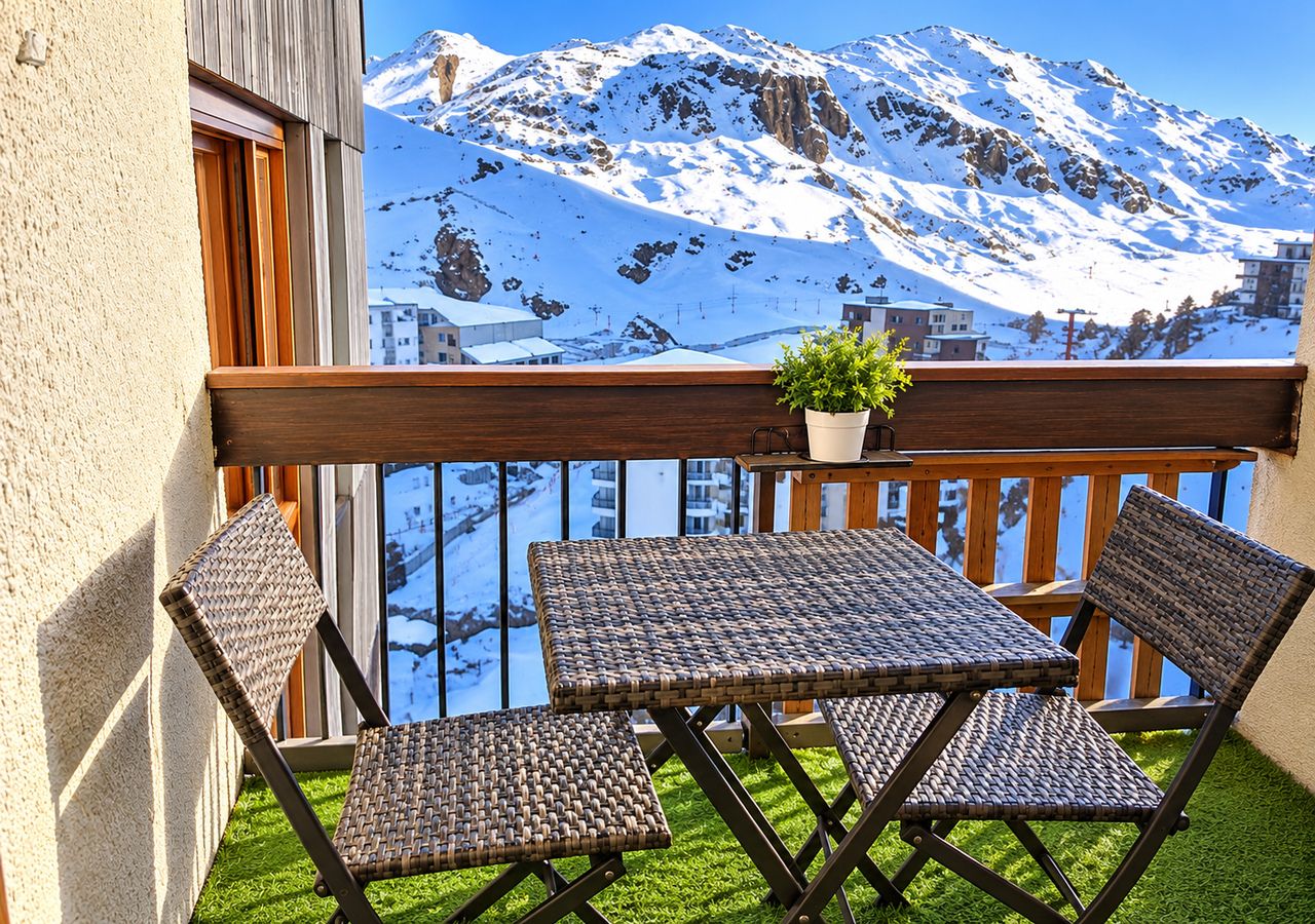 A balcony with a view of snow-covered mountains, a table, and two chairs.