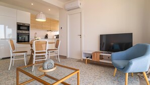 A modern living room with a TV, a blue chair, and a dining area with a chandelier. - Stunning apartment in Almuñecar (Almuñecar)