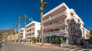 A multi-story hotel with balconies, a cafe on the ground floor, and palm trees lining the street. - Stunning apartment in Almuñecar (Almuñecar)