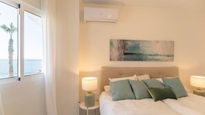 A bedroom with a bed, two bedside lamps, a painting, an air conditioner, and a window with a view of the sea. - Stunning apartment in Almuñecar (Almuñecar)