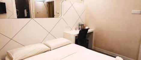 A hotel room with a bed, a desk, a chair, a mirror, and a small table.