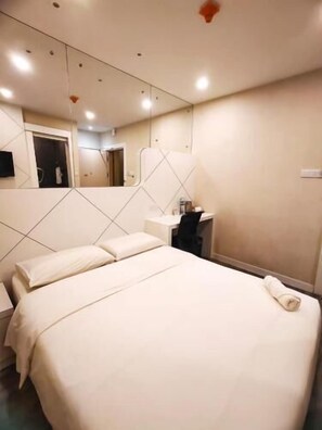 Una habitación de hotel con una cama, un escritorio, una silla, un espejo y una mesita.