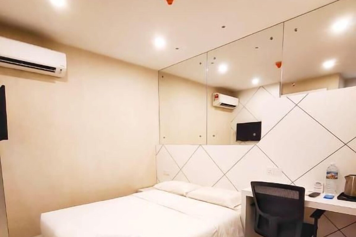 A hotel room with a bed, a desk, a chair, an air conditioner, and a tiled wall.