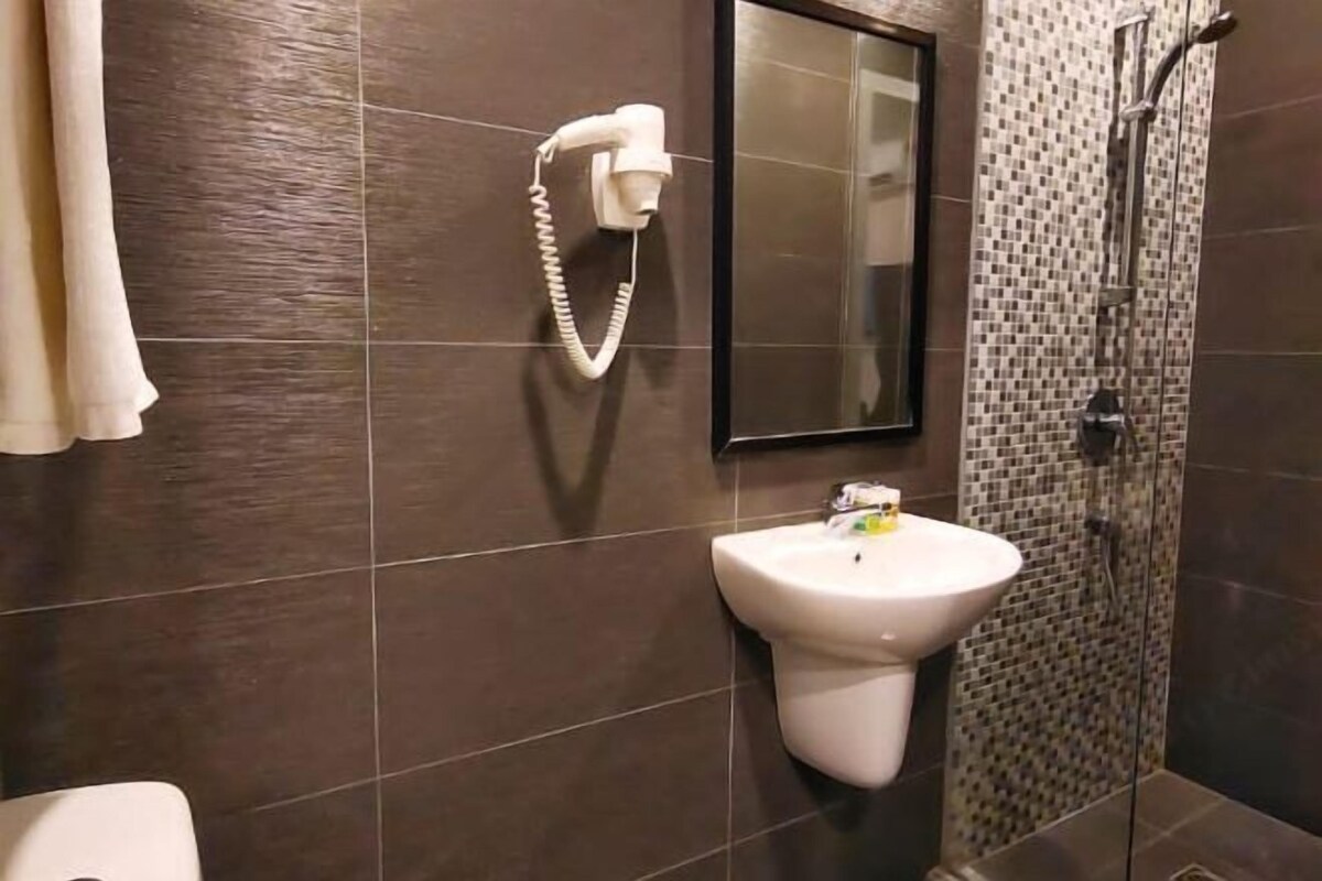 A bathroom with a sink, a mirror, a shower, and a telephone.
