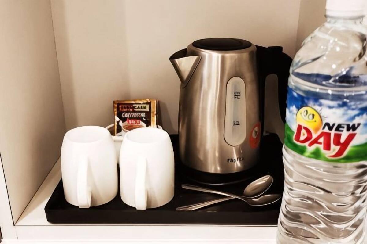 Uma cozinha compacta com chaleira, duas canecas, um sachê de leite, uma garrafa de água e uma colher.