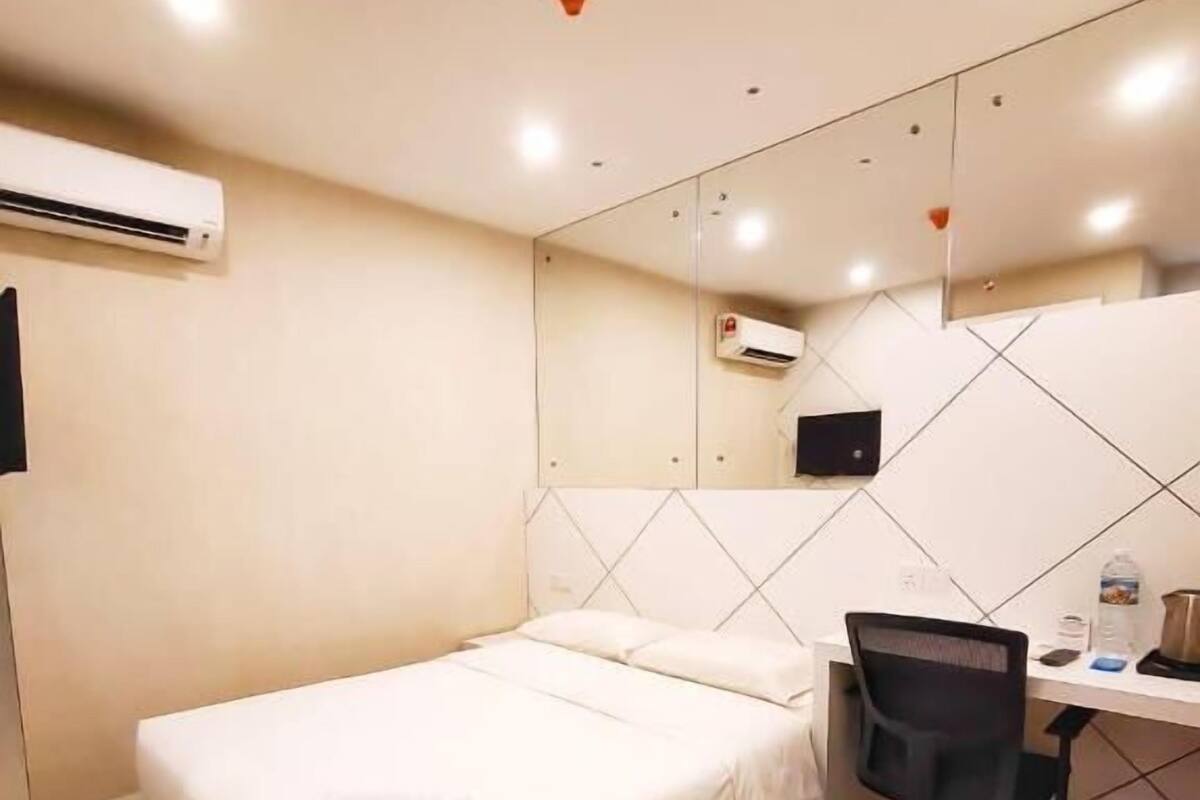 Quarto de hotel com cama, escrivaninha, cadeira, ar condicionado e parede revestida de azulejos.