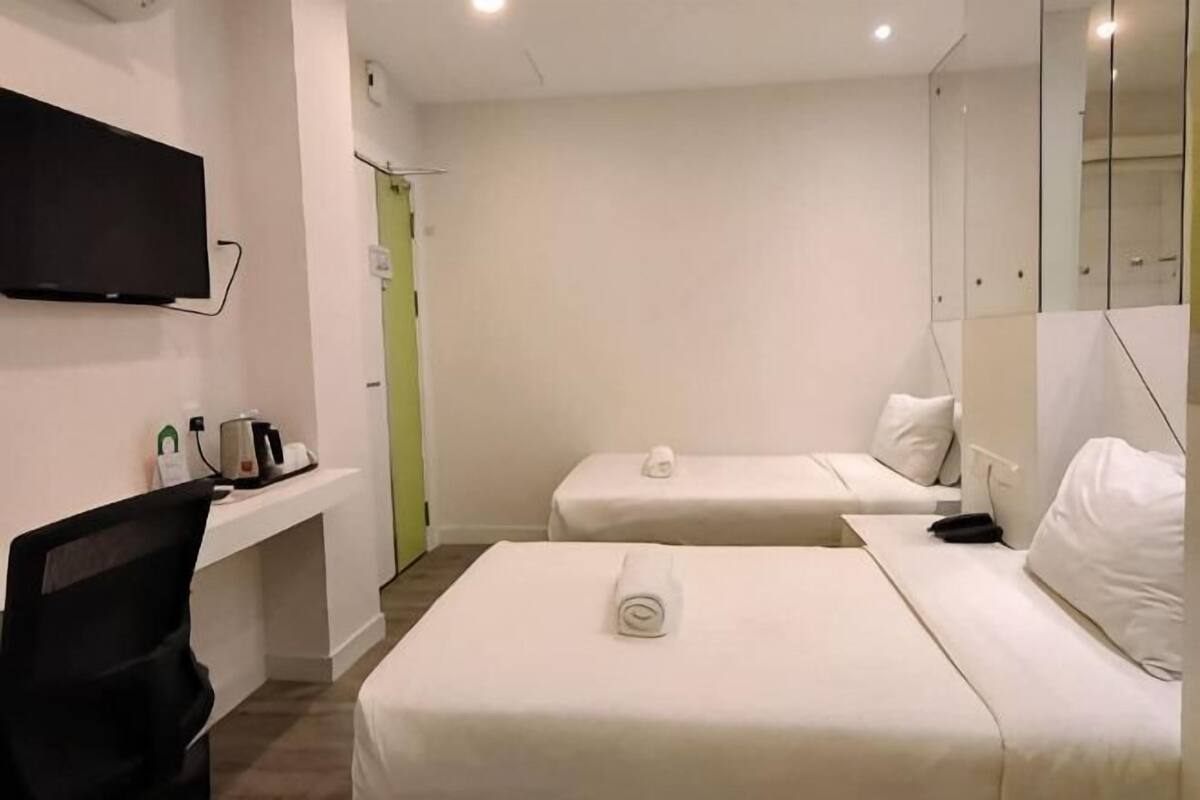 Quarto de hotel com duas camas, uma televisão, uma escrivaninha com cadeira e um espelho.