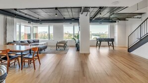 A spacious living area with a dining table, sofas, and a foosball table. Large windows offer views of the city. - Chic Urban 1BR Apt with Balcony and Skyline Views (Ottawa)