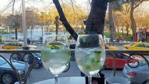 Uitzicht vanaf een tafel met twee glazen heldere drank, een metalen hekwerk en een parkeerplaats met gele taxi's en andere auto's.