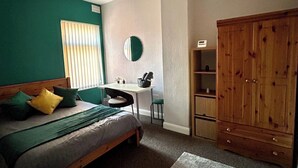 Ein Schlafzimmer mit Bett, Schreibtisch, Stuhl, Kleiderschrank und Spiegel.