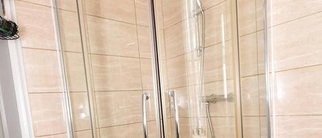 A glass-enclosed shower stall with a white base and a tiled floor.
