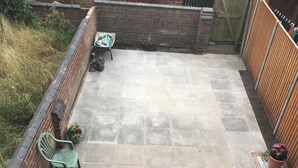 Eine Terrasse mit gefliestem Boden, einer Ziegelwand und einem Holzzaun.