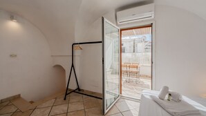 Una habitación de hotel con una cama, un ventanal que da a un área exterior, una pequeña mesa y una silla.