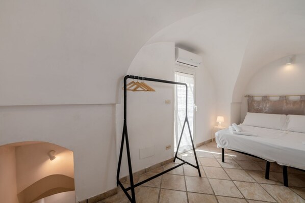 Quarto com cama, um cabideiro, mesa de cabeceira com abajur e teto em arco.