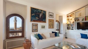 A living room with a white sofa, a glass coffee table, a bookshelf, and a large painting. - Lando House - Castellare de'Rossi (Siena)
