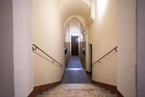 A narrow, stone-floored stairway with a central archway leading to a door at the top.