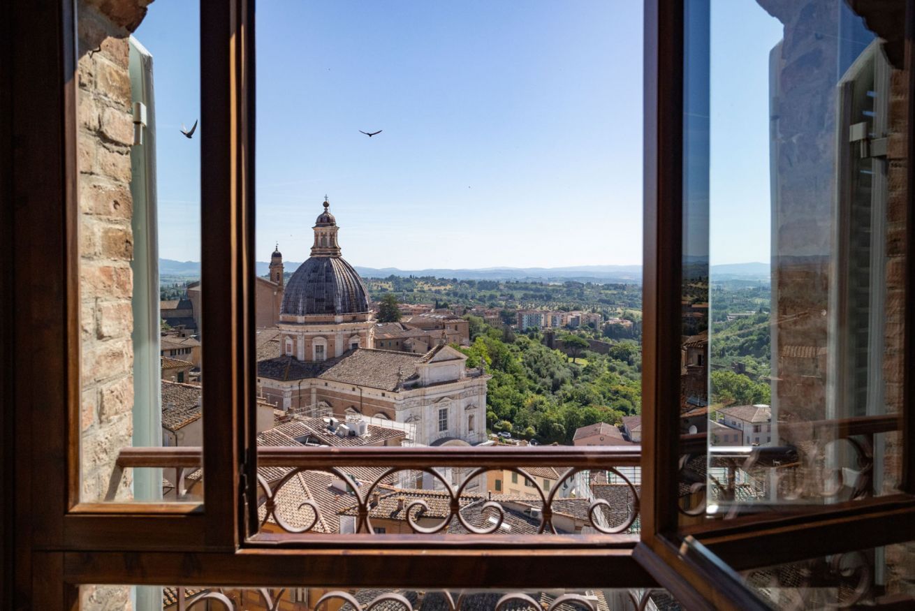 A view from a window with a metal railing, overlooking a cityscape with historical buildings and a prominent dome structure.
