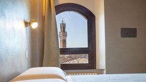 A hotel room with a bed, a window with a view of a tower, and a wall-mounted light fixture. - Lando House - Castellare de'Rossi (Siena)