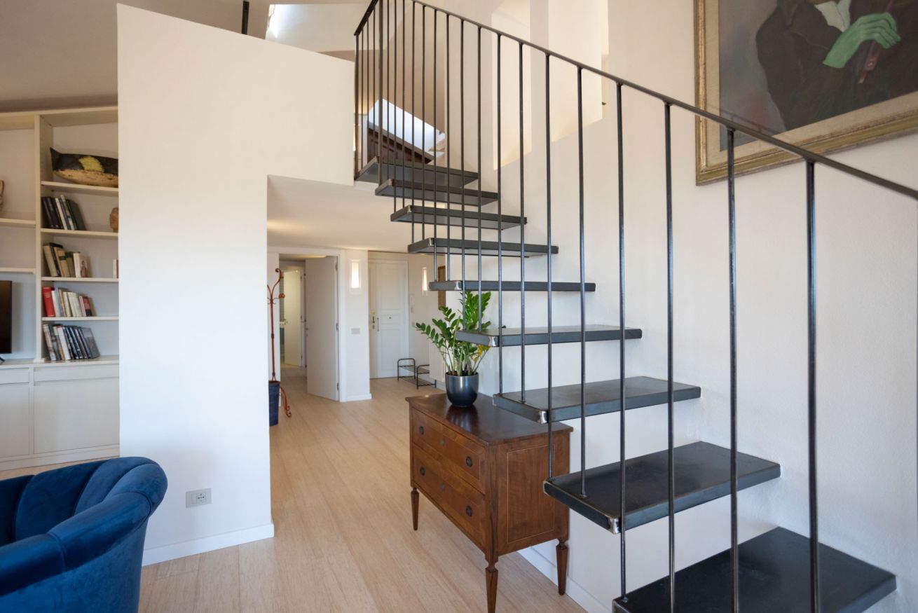 A modern staircase with a minimalist design, a wooden side table with a plant, and a blue chair in a bright, open living space.