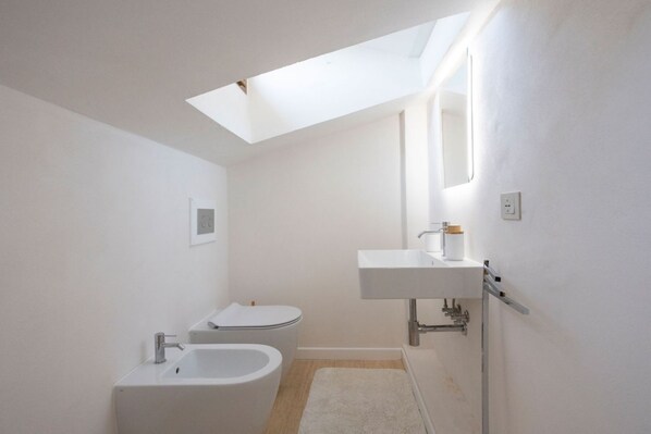 A modern bathroom with a skylight, a bathtub, a toilet, and a sink. - Lando House - Castellare de'Rossi (Siena)