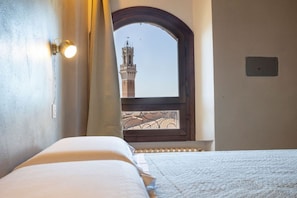 A hotel room with a bed, a window with a view of a tower, and a wall-mounted light fixture.