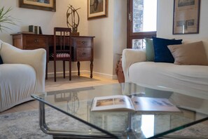 A living room with a glass coffee table, two sofas, a wooden side table, and a chair.