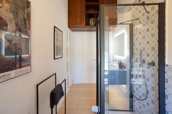Un baño moderno con cabina de ducha de vidrio, un mueble de madera sobre el lavamanos y obras de arte en las paredes.