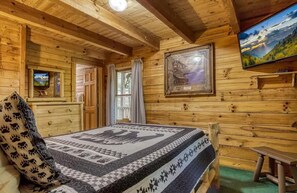 A wooden cabin interior with a bed, a television, and framed pictures on the walls. - Pet Friendly Cabin w/ Hot Tub & Multicade (Sevierville)