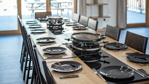 A dining area with a long table set for multiple people, equipped with a grill, plates, cutlery, and a hanging light fixture.