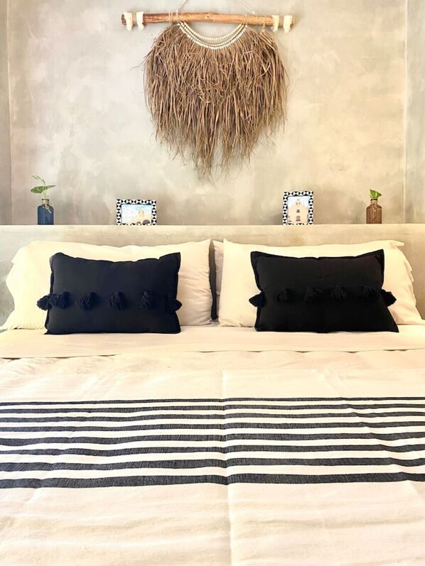 A bed with two black pillows, a striped blanket, and a wall-mounted macrame piece.