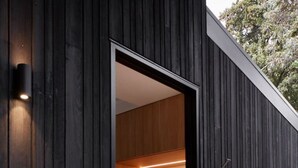 A modern building with a dark exterior, a door leading to a room with a bench and a coat rack. - Ukiyo House “The Floating World” (Port Willunga)