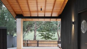 A covered outdoor area with a wooden ceiling, a concrete pillar, a view of trees, and a door with a circular window. - Ukiyo House “The Floating World” (Port Willunga)