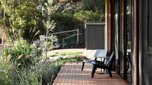 A wooden deck with a bench, surrounded by greenery and a metal fence. - Ukiyo House “The Floating World” (Port Willunga)