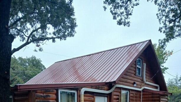 A small log cabin with a metal roof, a front door, and a patio area with a table and chairs. - Fun Cabin in the Woods (Longdale)