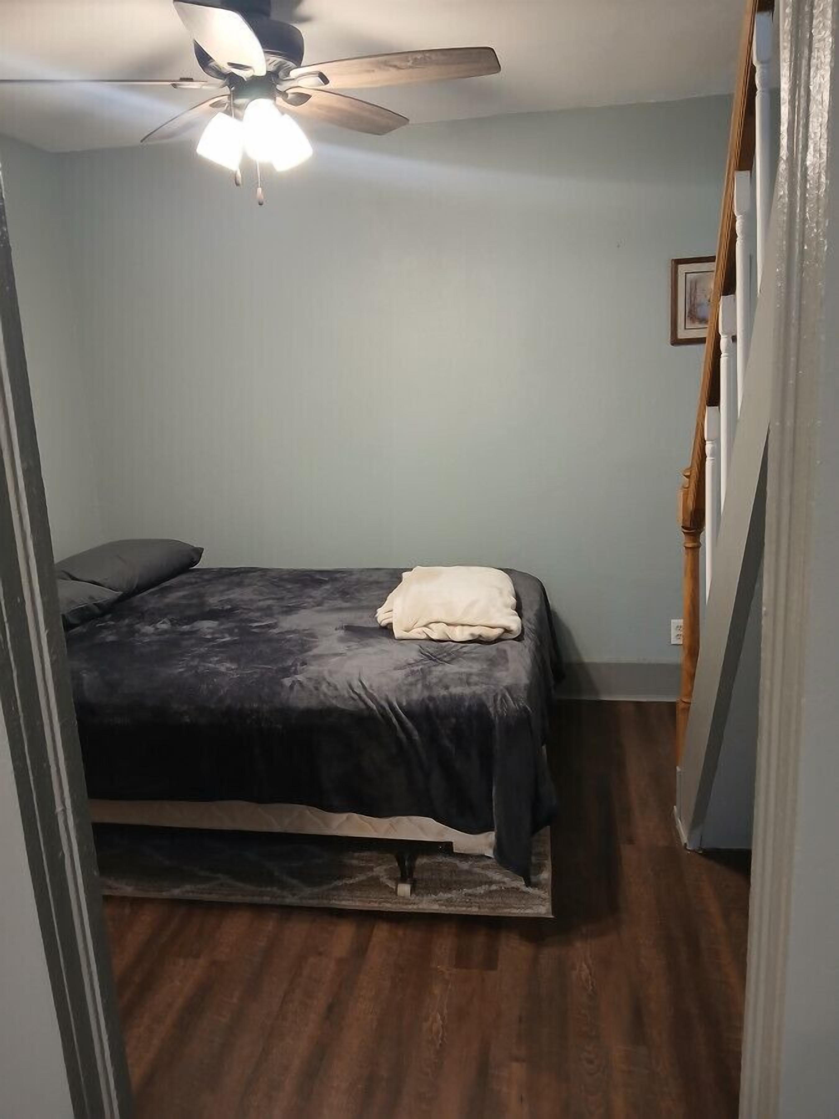 Een slaapkamer met een bed, een plafondventilator en een houten vloer.