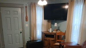 A living room with a brown leather sofa, a television mounted on the wall, a ceiling fan, and a wooden table with chairs. - Fun Cabin in the Woods (Longdale)