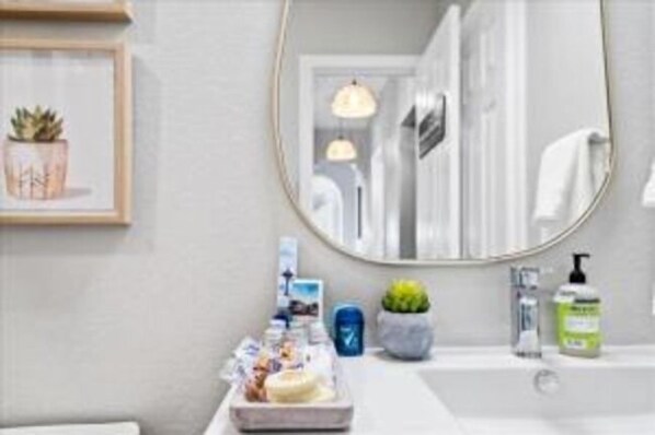 A bathroom with a round mirror, a sink, a small potted plant, and toiletries on the counter. - Luxe Farmhouse Hot Tub Pool On 5 Acres (Manor)