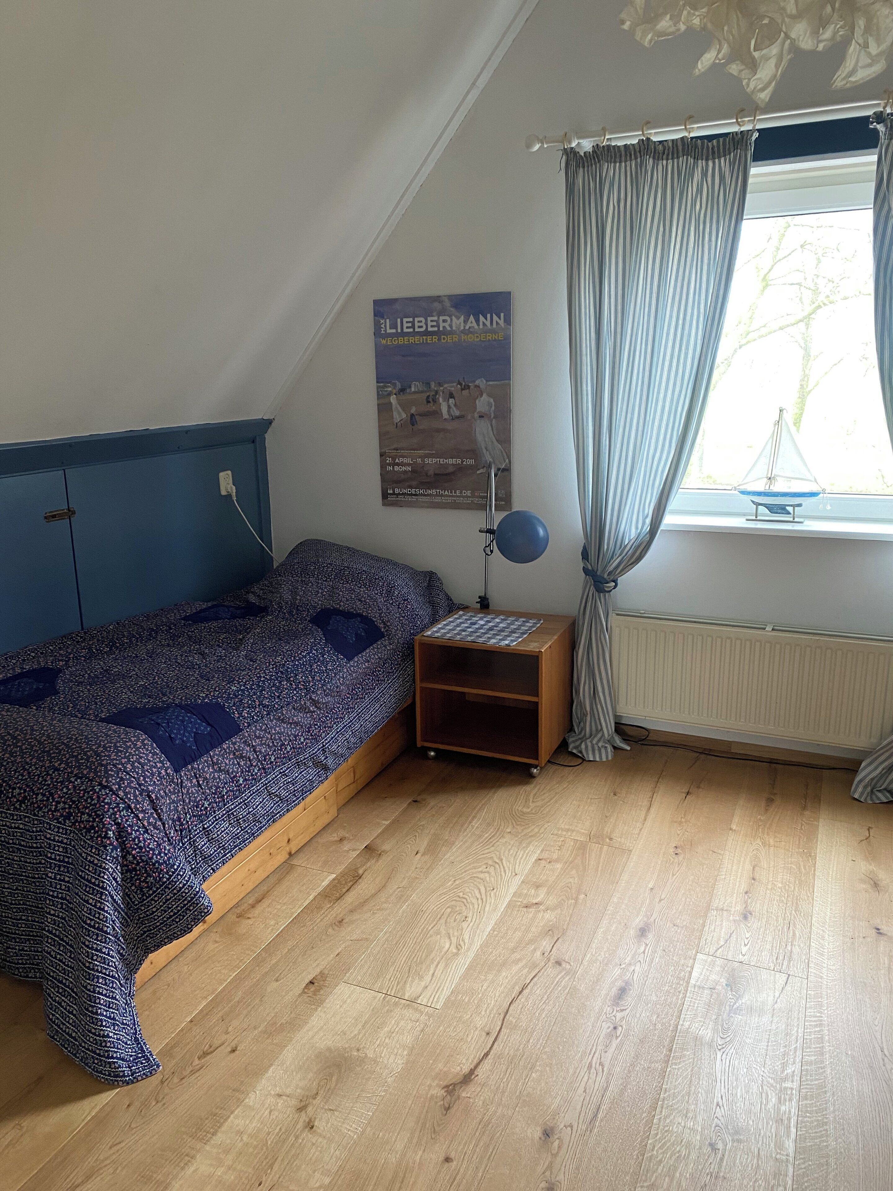 Une chambre avec un lit superposé, une petite table de chevet avec une lampe, une affiche accrochée au mur et une fenêtre avec des rideaux.