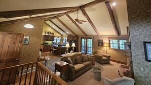 A spacious loft with exposed wooden beams, a cozy living area with a sofa and armchairs, a kitchen with a central island, and large windows providing natural light.