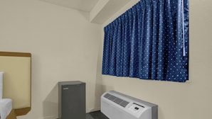 A hotel room with a bed, a gray air conditioner, and a window with blue curtains. - Brookville Inn By OYO Near Dayton International Airport (Brookville)