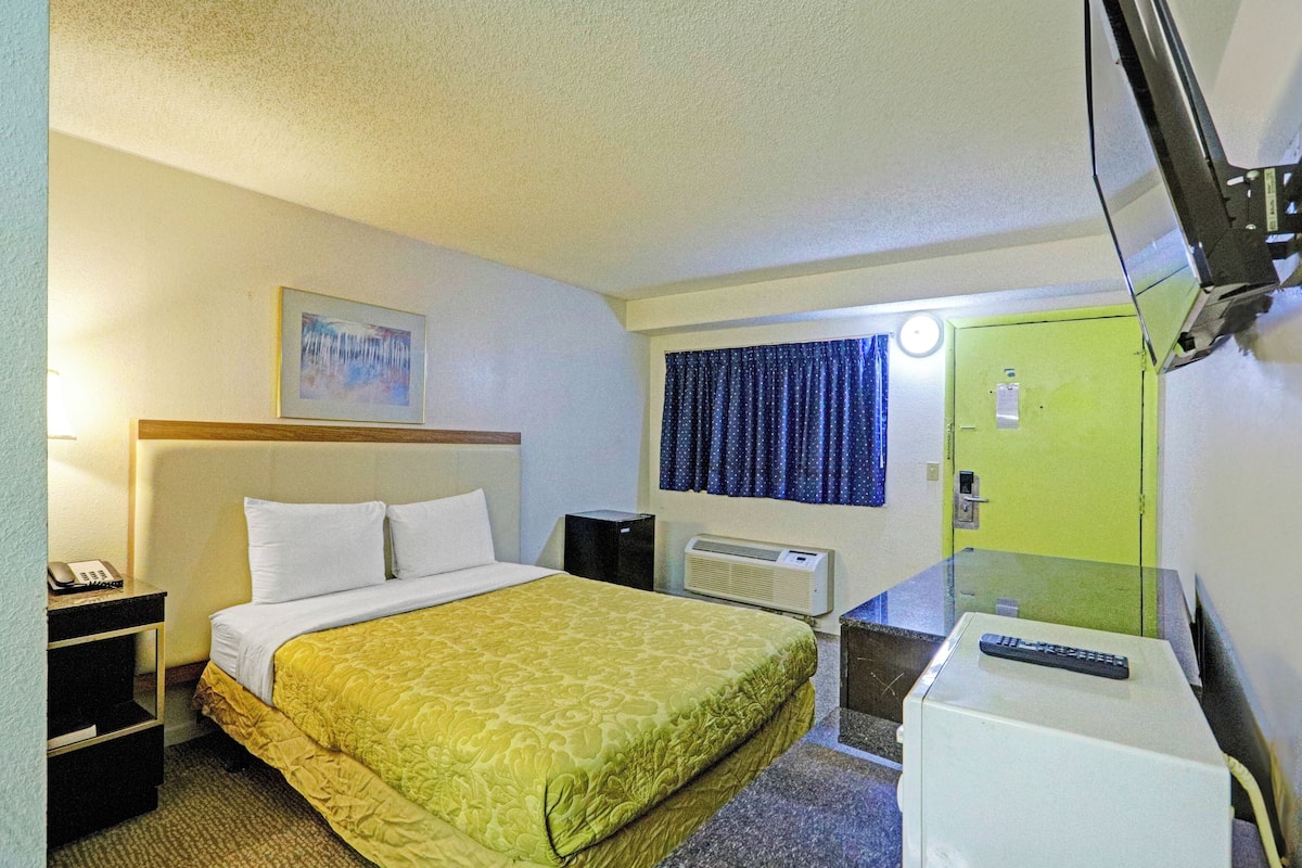 Ein Hotelzimmer mit Bett, Schreibtisch, Telefon, Fernseher und einer grünen Tür.