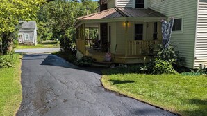 Une maison à deux étages avec un porche, une cheminée et une allée menant à une petite maison séparée.