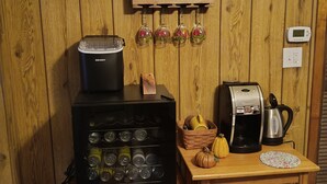 Une cuisine équipée d’une machine à café, d’une bouilloire, d’un réfrigérateur à vin et d’une étagère où sont rangées des bouteilles et des verres.