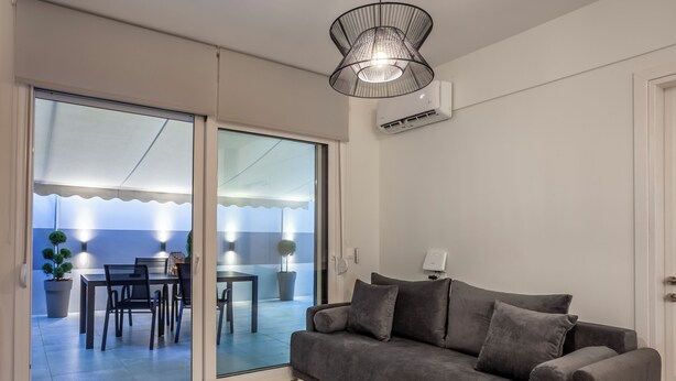 Una sala de estar moderna con un sofá gris, una mesa de centro de madera y un ventanal corredero que da a un balcón con zona de comedor.