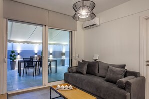 Ein modernes Wohnzimmer mit einem grauen Sofa, einem Holztisch und einer Schiebetür zu einem Balkon mit Essbereich.