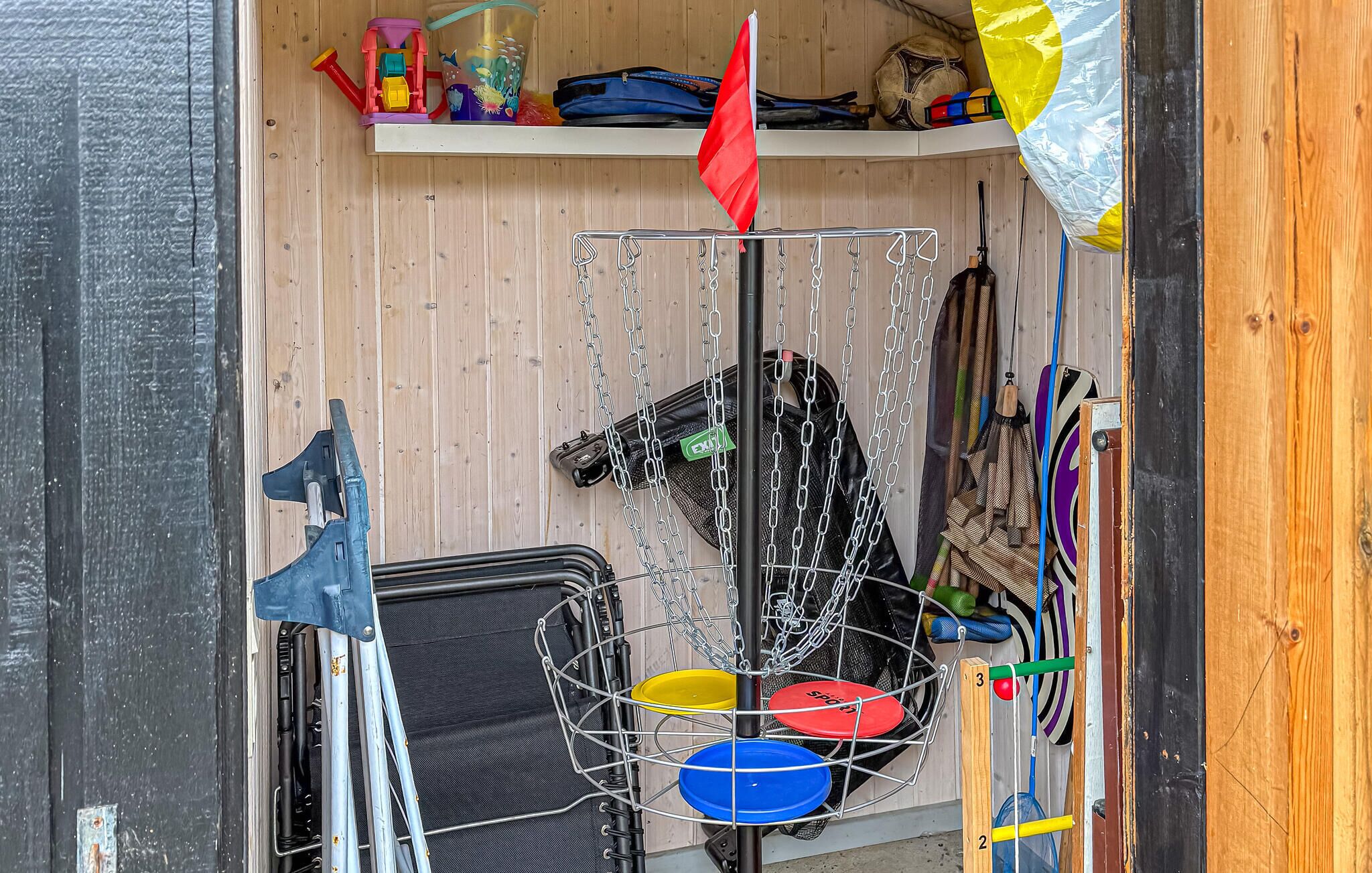Un cesto de disc golf con tres canastas, una escalera y varias bolsas y equipos sobre estantes.