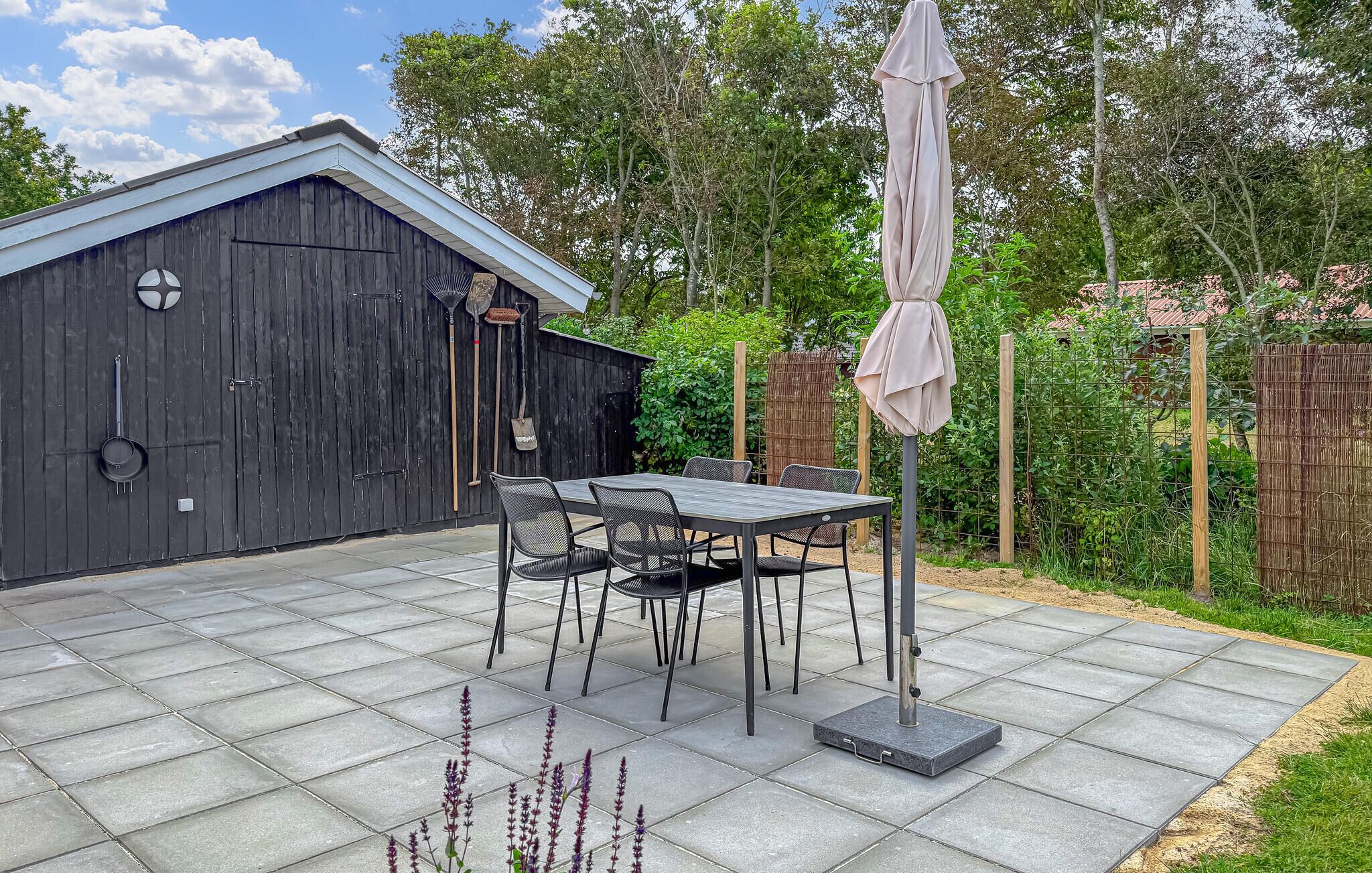 A patio with a table and chairs, a covered umbrella, and a wooden fence in the background.