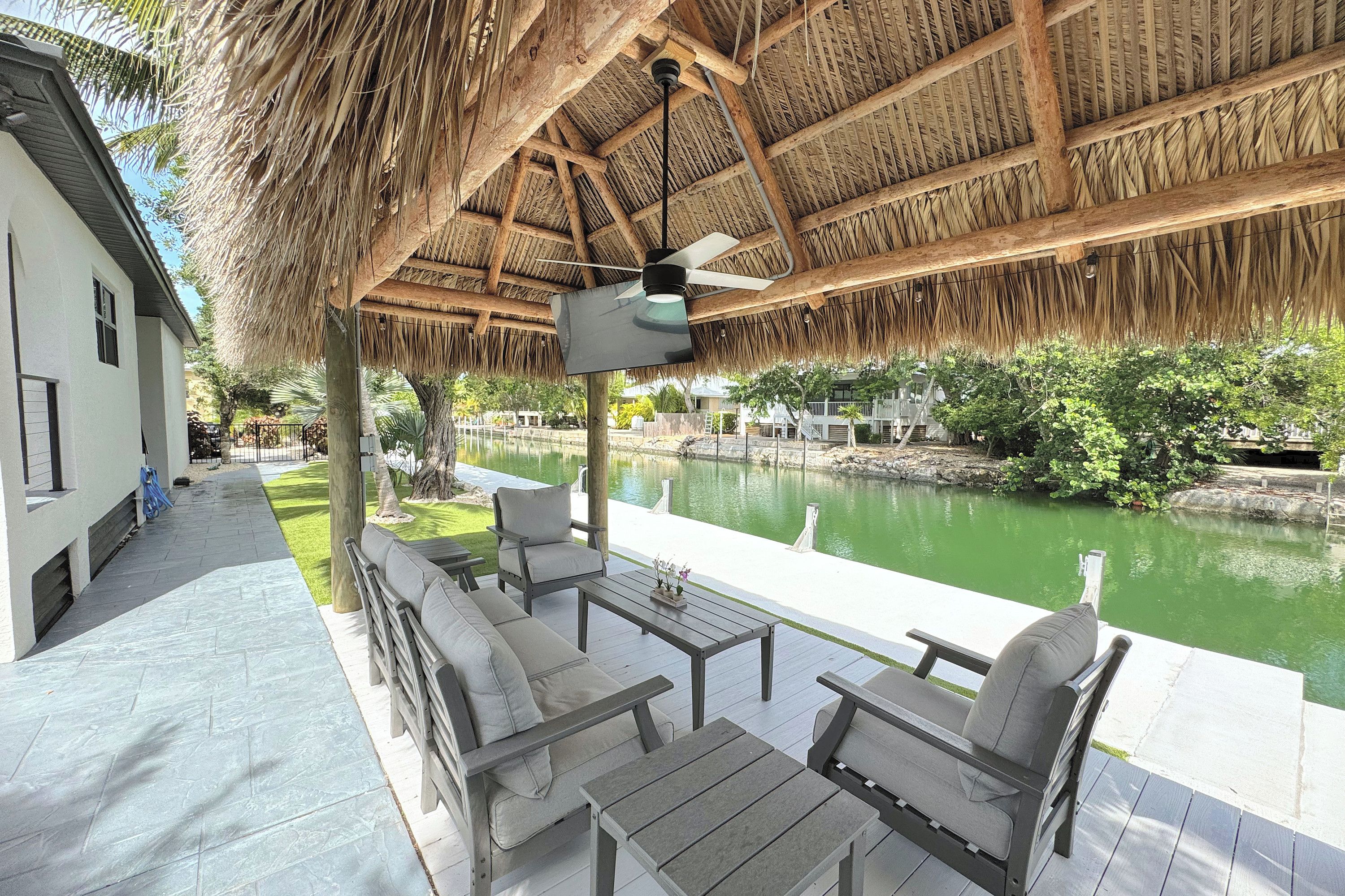A covered outdoor seating area with a pool view, featuring a thatched roof and wooden furniture.